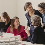 Das Team von Weiter Schreiben sitzend und stehend an einem Schreibtisch
