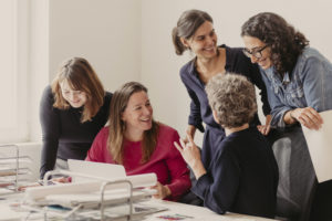 Das Team von Weiter Schreiben sitzend und stehend an einem Schreibtisch