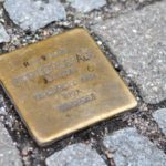 Ein Stolperstein zwischen grauen Steinen eines Bürgersteigs