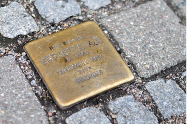 Ein Stolperstein zwischen grauen Steinen eines Bürgersteigs