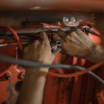 Nahaufnahme von zwei Händen, die an einem Motor arbeiten; Geschichte eines Geflüchteten