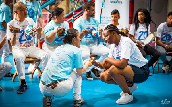 Doch wie spielt man nun Capoeira? Für ein Spiel (jogo) finden sich alle Capoeiristas in der Roda zusammen: ein Kreis, an dessen Kopf sich die Bateria befindet: die Sänger*innen und die Instrumente. Von dort treten zwei Capoeiristas in das Spiel ein: sie knien vor der Berimbau nieder, geben sich die Hände und beginnen das Spiel gewöhnlicherweise mit einem Aú (einem Radschlag) oder einem Rolê (Drehung um sich selbst).
