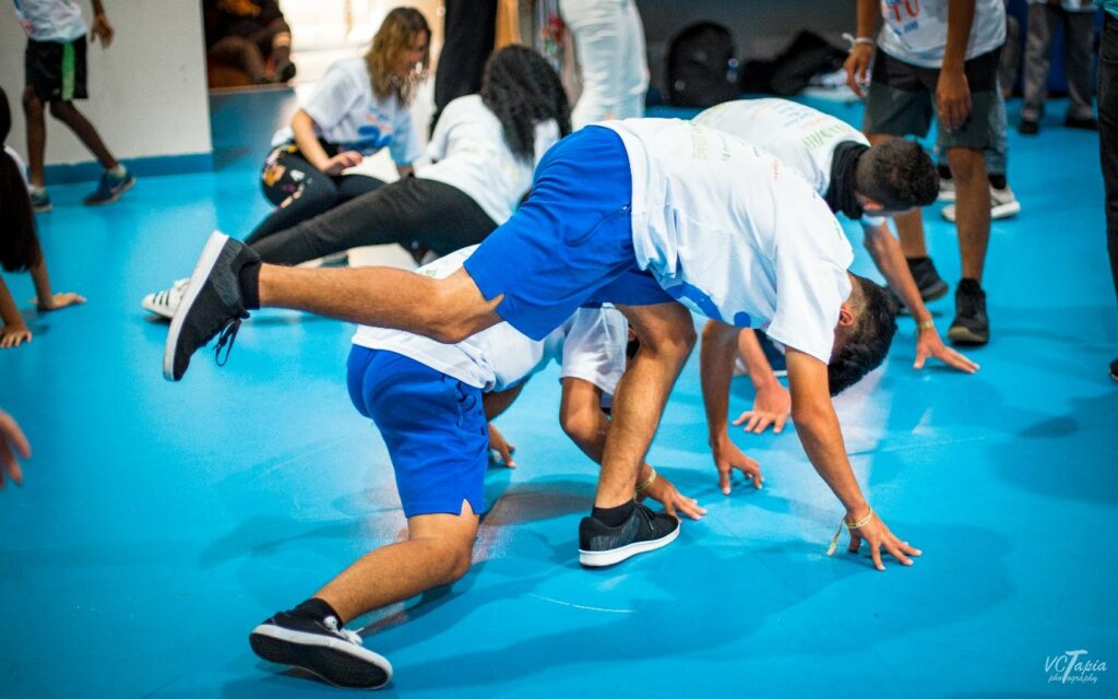 Die beiden Capoeiristas „spielen“ (jogar) etwa 3-4 Minuten miteinander, bis der*die nächste Capoeirista das Spiel „kauft“ (comprar): er*sie kniet am Eingang der Roda und bringt sich mit ausgestrecktem Arm in das Spiel mit der Person ein, die zuletzt in die Roda eingetreten ist. Klingt kompliziert? Ist es eigentlich gar nicht, ein Beispiel einer Roda könnt ihr euch hier anschauen: //www.youtube.com/watch?v=j0wnYgPXjrE
